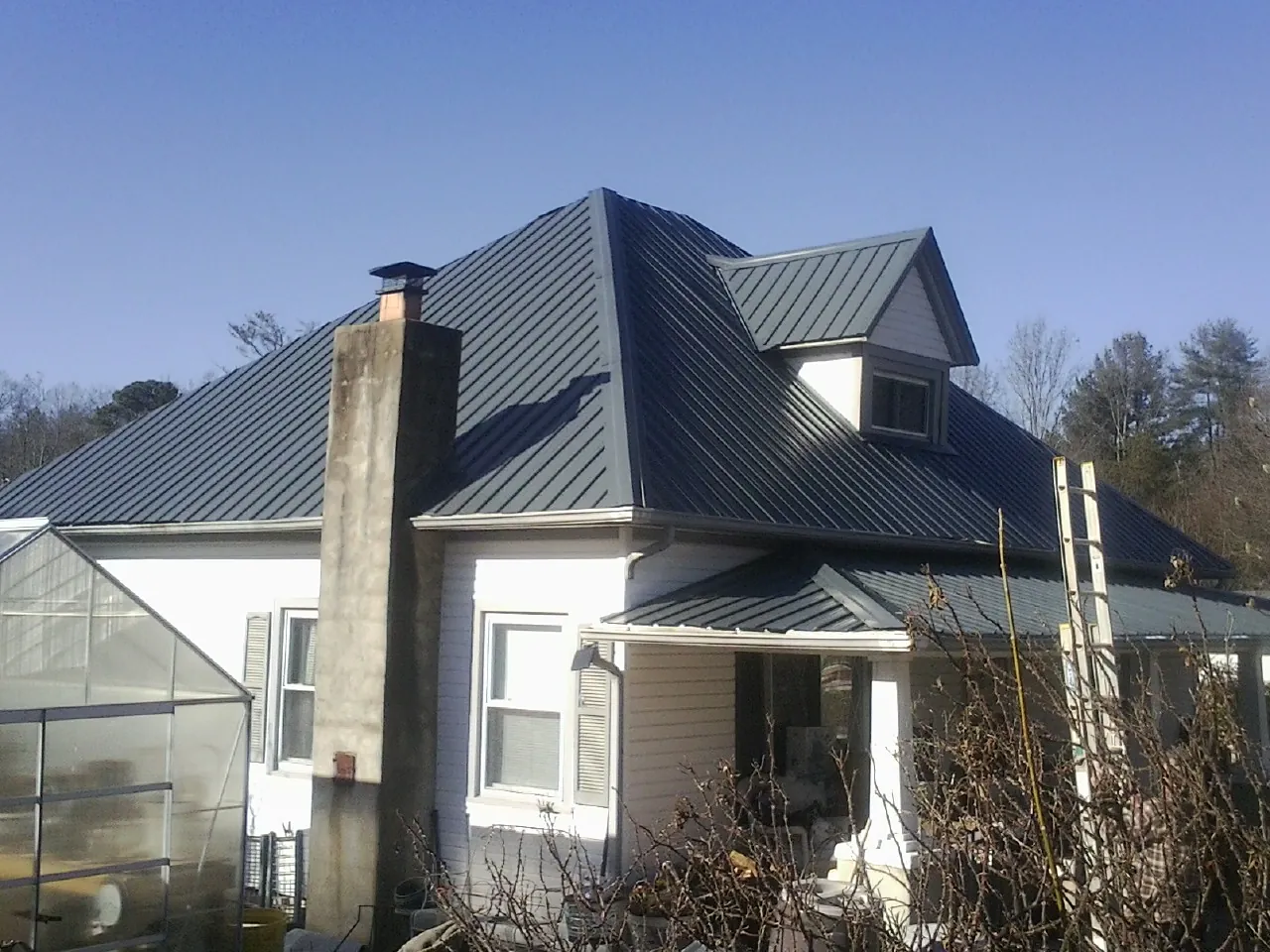 Dark blue standing seam metal roof on a white farmhouse with dormer — Slate & Tile Roof Repair by Roofing Brothers in Gerber
