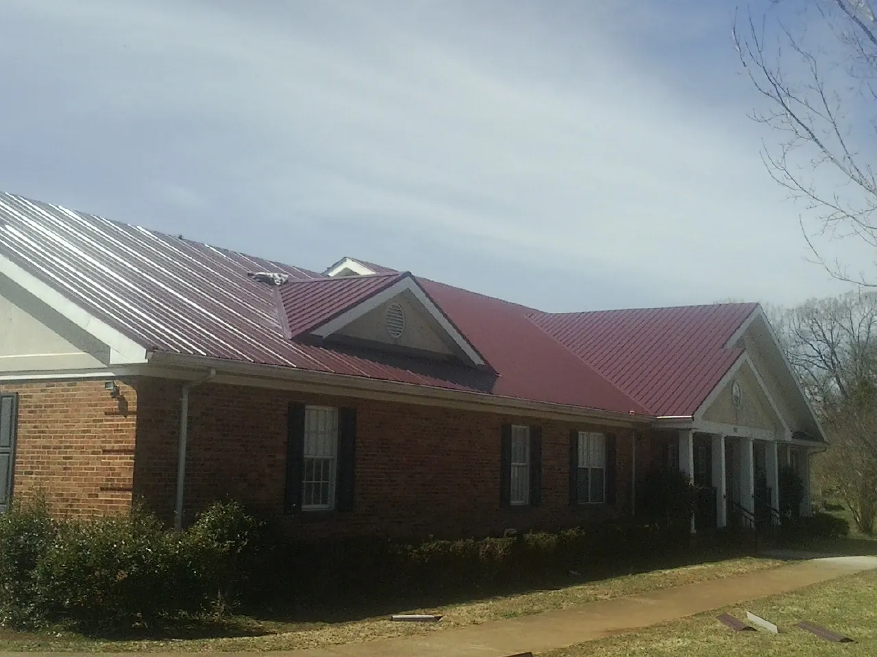 Red metal roof with gabled entries on a long brick building, from a Hail Damage Roof Repair job in Gerber