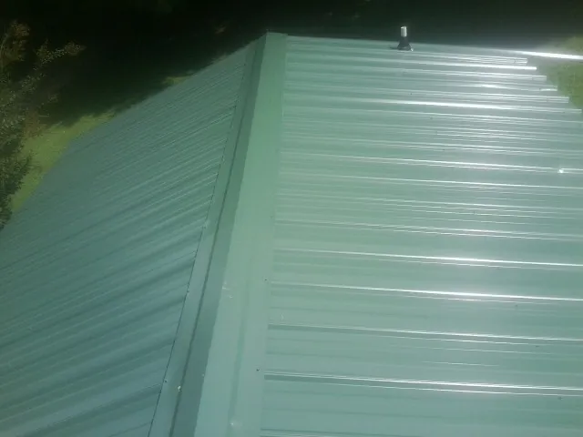 New green metal panels meeting at the ridge of a roof — Flat Roof Repair work by our crew in Gerber