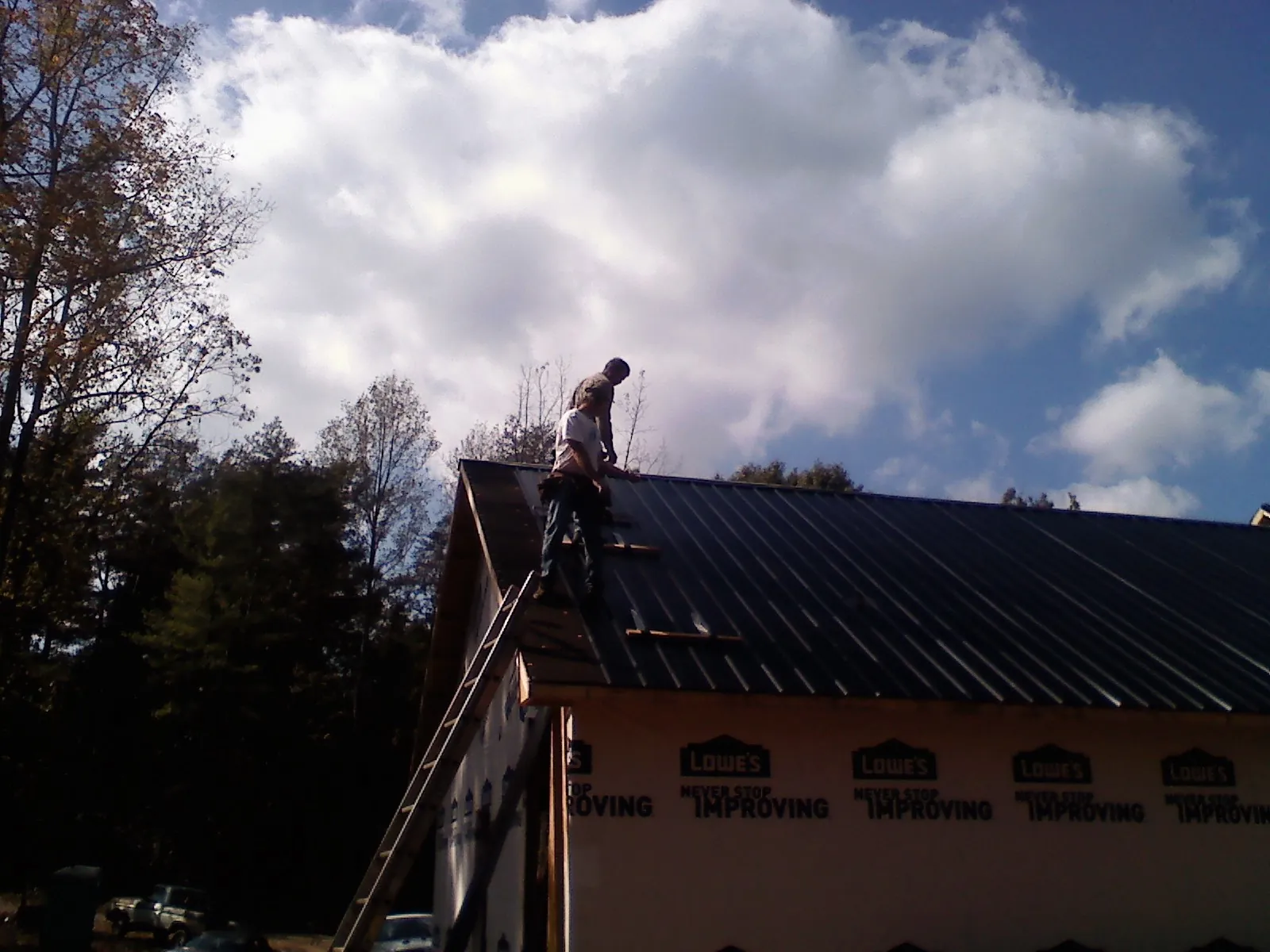 Roofer fastening dark metal panels high against a cloudy sky, from a Roof Inspection job in Gerber