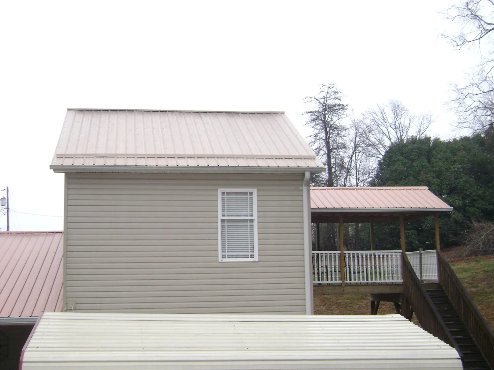 Tan metal roofs on a two story addition and attached porch, from a Roof Replacement job in Gerber